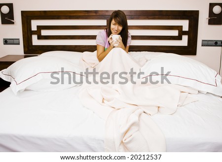Young woman in bed enjoying a coffee in a huge bed