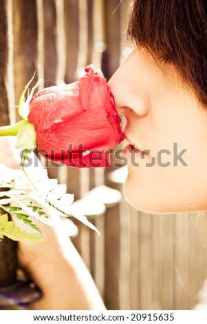 Young anonymous woman smelling a red rose behind metal fence.