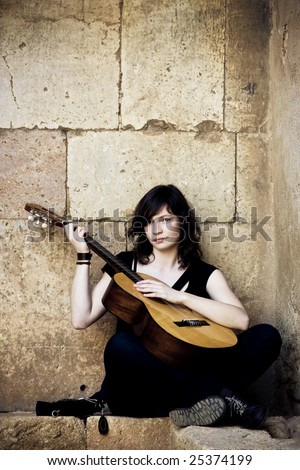 Young guitar performer against brickwall