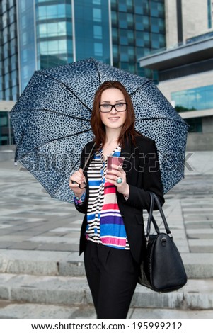 Secretary under an umbrella with a coffee and a bag on the building background