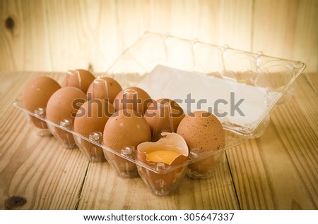 A dozen of eggs in carton, one broken and exposing the yolk