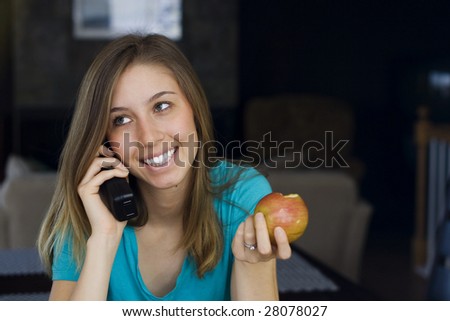 Beautiful young woman talks on the telephone while eating an apple at home.