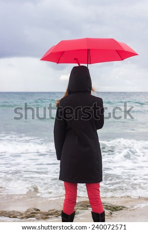Woman with red umbrella looking at sea