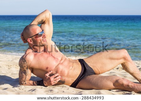 Muscular man in swimwear relaxing sunbathing on sea beach at summer