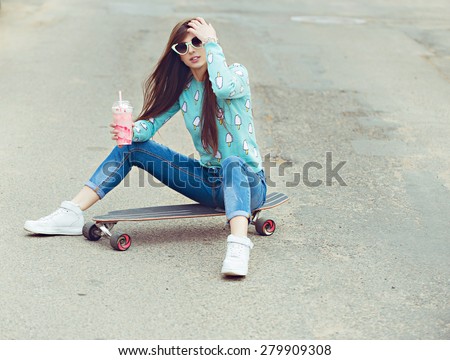 Beautiful young woman posing with a skateboard seat on skate, street fashion lifestyle. Keep cocktail and make selfie photo