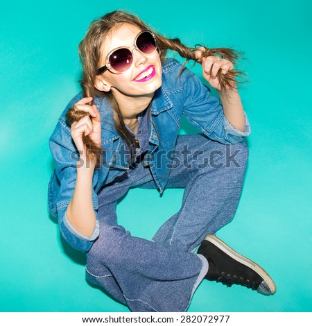 Emotional pretty young hipster girl in sunglasses make funny face and keep hairs in hand on blue background