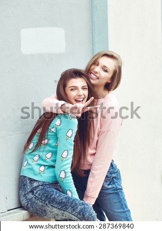 two fashion hipster girlfriends are hugging and having fun in city grunge background