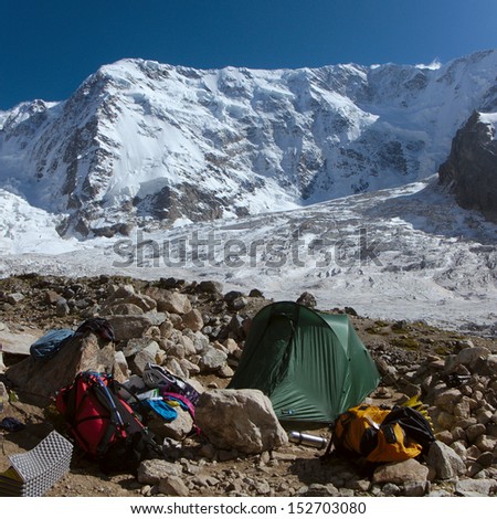 High altitude bivouac with tent, backpack and mountaineering gear with mountains with snow and glaciers in the background