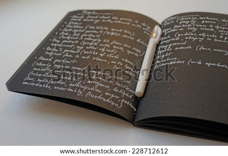 Notebook with black paper and white pen opened with written white on black text