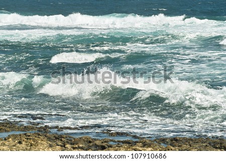 Deep blue ocean waves white with foam roll on rocky shore.