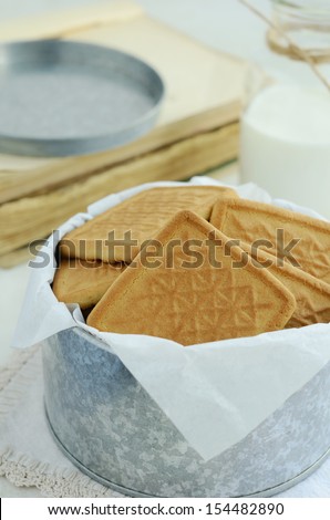 Heap of crumbly cookies packed with parchment paper in round tin box on light background