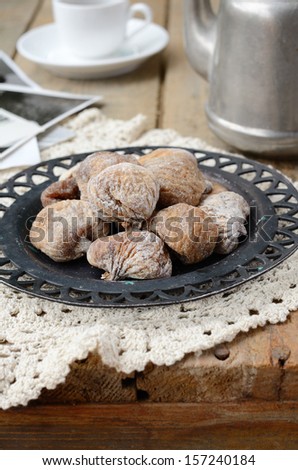 Still life with sun dried figs on metal plate, vintage coffee pot, coffee cup and retro shots on wooden background