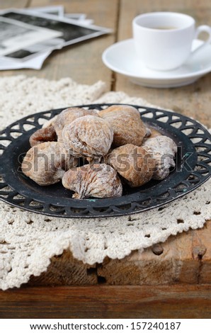 Still life with sun dried figs on vintage metal plate, coffee cup and retro black and white shots on wooden background