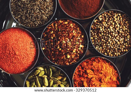 Rack with traditional indian spices for cooking - green cardamom, turmeric powder,  coriander seeds, cinnamon, cumin, and chili pepper