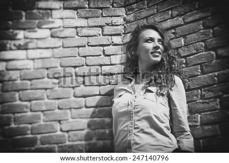 Pretty young city girl standing against an exterior brick wall. Black & white pictures.