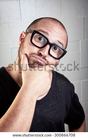Wondering kind man with glasses. Unshaven guy with wide eyes and mouth open looking at the camera. The hand rubs chin. Portrait over textured background.