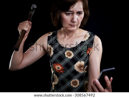 Middle aged woman, in despair smashes the laptop. Furious woman face. Black background.