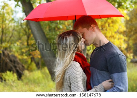 young couple man and woman kiss under red umbrella  in autumn