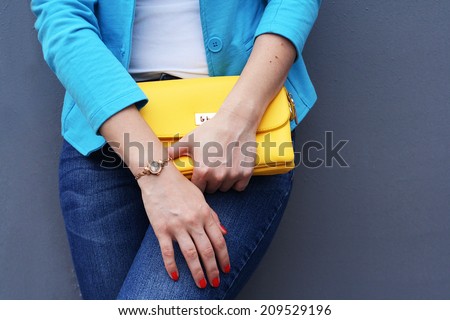 The fashionable young woman  holding yellow handbag clutch gray background