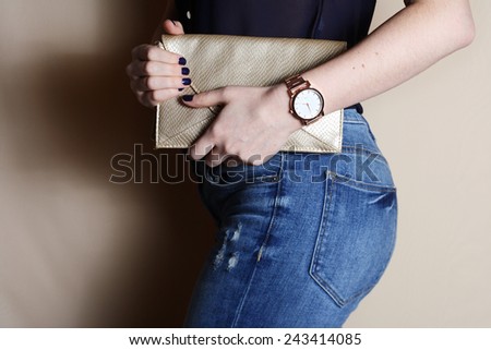 Stylish woman in jeans with small gold handbag clutch and watch . fashion concept.