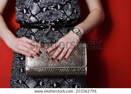 Fashionable beautiful woman with gold clutch purse in her hands and snake evening dress