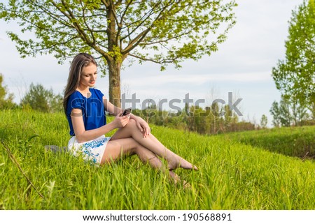Woman sitting in grass under tree with phone