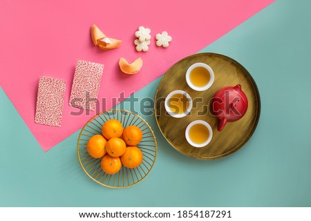 Group of Chinese New Year tea, red envelopes, tangerine and decorative items objects on light blue and pink background.
