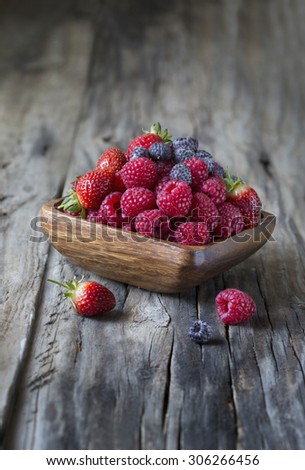 Raspberry and other berries in wooden bowl on rustic wooden table top. Stylized fruit shot.