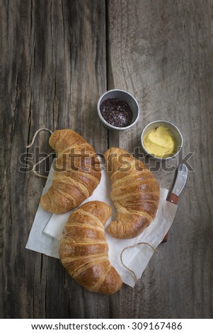 Freshly baked french croissant served with jam and butter on rustic wooden table top. Over head text space image.