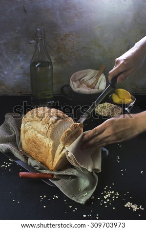 Freshly baked oat bread loaf being sliced in moody rustic bakery kitchen. Table top shot.