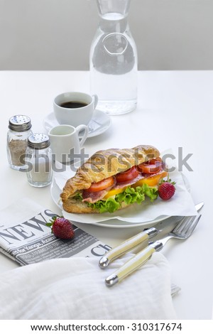 French loaf Cheese and ham sandwich served with espresso coffee and newspaper on white table top.
