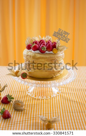High vintage naked cake with fresh juicy strawberry on glass cake stand on yellow background.