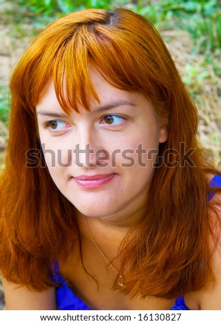 Portrait of the woman with red hair in dark blue clothes against green plants