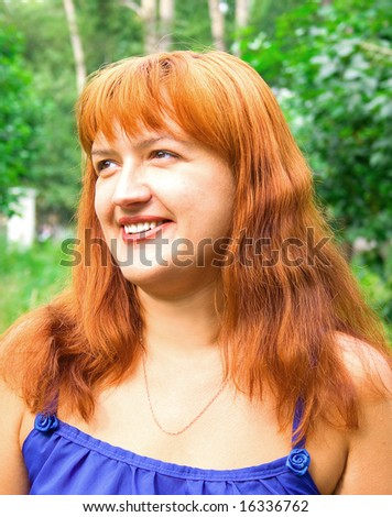 Portrait of the smiling women with red hair in dark blue clothes against green plants