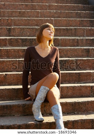 The romantic girl dreams and smiles, sitting at ladder steps. Outdoor, park