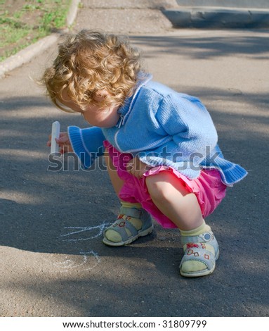 The little girl draws a chalk on asphalt in park