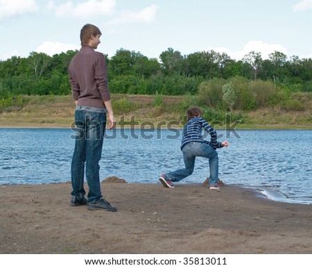 Young men throws stone into the river against summer landscape