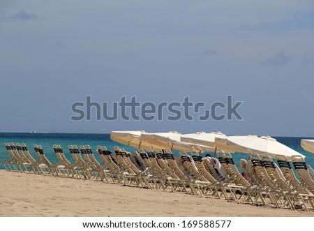 Row of black and white lounge chairs and big shade umbrellas on hot sandy beach at tropical resort invites vacationers to unwind at the shoreline.