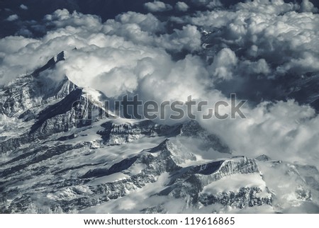 The jagged peaks of the mountain range appear through the clouds blocking their flow