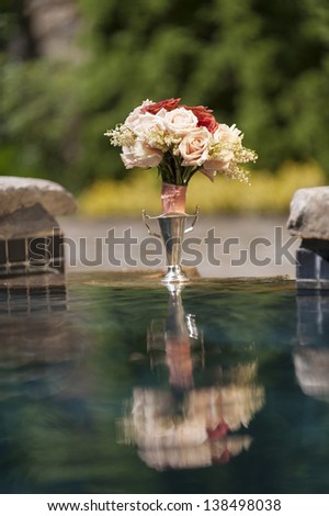 A bouquet of red and pink roses and it\'s reflection sitting on the edge of a pool.