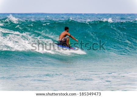 KOLOA, KAUAI, HI - APRIL 24, 2008 - Young man riding a boogie board in a blue wave in the summer.