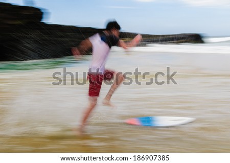 Young man running and jumping on a skim board in shallow water on a sandy beach in Maui, Hawaii, USA