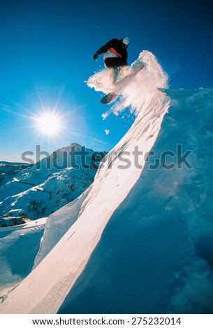 Snowboarder jumping off a cliff off piste, backlit by the sun on a sunny day in Donner Pass, California, USA.