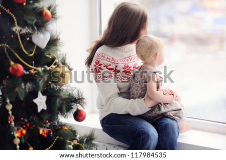 Mother with baby sitting by the window. Christmas decorations. On Christmas, waiting for a miracle. A woman with a child looking out the window.