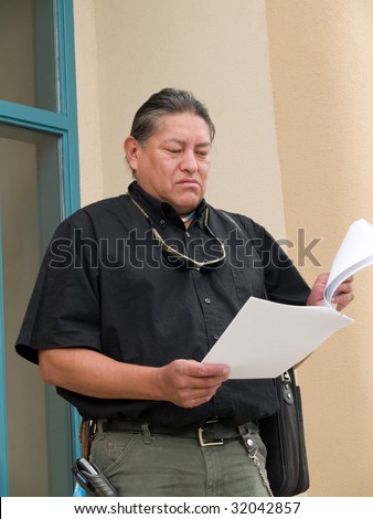 Native American man stepping out of an office building and reading papers.
