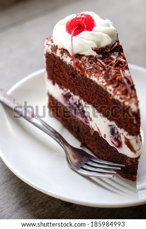 Dark chocolate cake topping with cherry and whipping cream placed on wood background