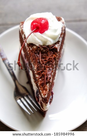 Dark chocolate cake topping with cherry and whipping cream placed on wood background