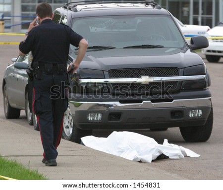 A policeman makes a cell call while standing beside a shooting victim.