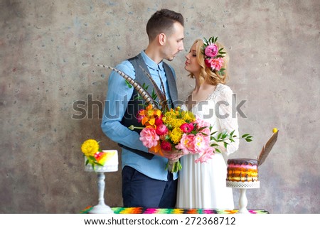 Young wedding couple against texture wall and table with small cakes