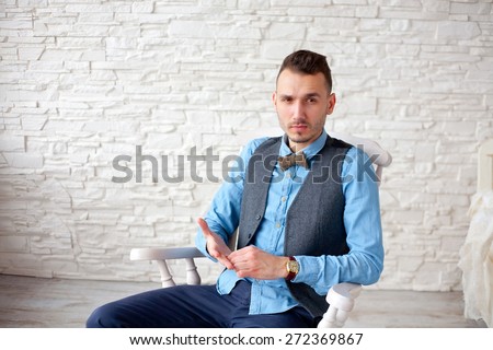 young business man sitting on a chair with serious expression on a background of white brick wall